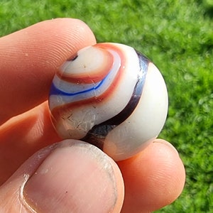 Może przedstawiać: Biała szklana kulka z czerwonymi, niebieskimi i czarnymi wzorami w kształcie spirali.