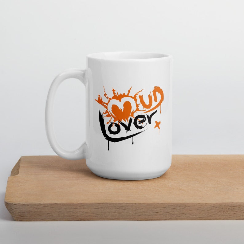May include: White ceramic mug with a black and orange graphic that says "Mud Lover" with a heart shape in the middle.