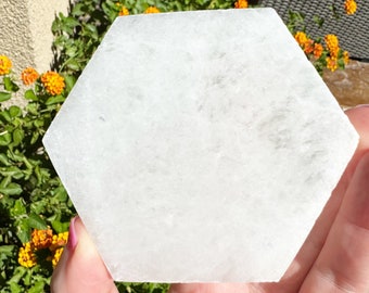 May include: A white hexagonal selenite charging plate. The plate is smooth and polished, with a slightly cloudy appearance.