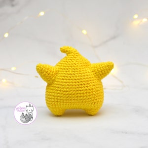 Puede incluir: Un juguete de peluche de color amarillo en forma de estrella tejido a crochet. El juguete est&aacute; sobre una superficie de m&aacute;rmol blanco.