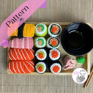 Peut inclure: Un ensemble de sushis en crochet sur un plateau en bois. Les sushis sont faits dans différentes couleurs et motifs, y compris le rose, l'orange, le jaune, le vert et le rouge. Il y a un petit bol de sauce soja et des baguettes sur le plateau. Le plateau porte le texte "Agellia Crochet".