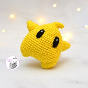 Puede incluir: Un juguete de peluche amarillo de crochet con forma de fantasma con ojos negros. El juguete est&aacute; hecho con un hilo suave y texturizado y tiene una forma redondeada y bulbosa.
