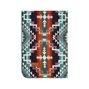 Puede incluir: Una manta de lana con un diseño geométrico en verde, naranja, blanco y negro.