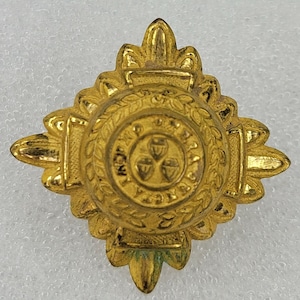 Könnte beinhalten: Goldfarbener, sternförmiger Anstecker aus Metall mit einem runden Design in der Mitte. Das mittlere Design zeigt drei Eicheln und einen Kranz aus Blättern.