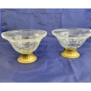 May include: Two clear glass bowls with a crackled finish and gold metal bases. The bowls are on a blue background.