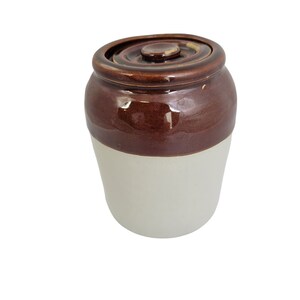 May include: A brown and white ceramic jar with a lid. The jar has a brown top and a white bottom.