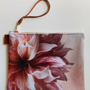 May include: A blush pink floral print canvas clutch with a brown leather strap.