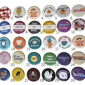 May include: A collection of thirty circular pin-back buttons arranged in five rows of six. Each button features unique colorful illustrations and text including phrases like 'Stay Positive', 'Mental Health Matters', 'You Are Enough', and 'Therapy Is Cool'.