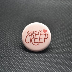 May include: Pink button with the text "beat it CREEP" in red lettering and a small red heart.
