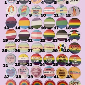 May include: A collection of 48 round buttons with various LGBTQ+ pride flags, slogans, and designs. The buttons are arranged in a grid pattern on a light purple background.