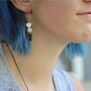 May include: A pair of earrings with a white heart charm, a pink bead, and black beads hanging from a gold hook.