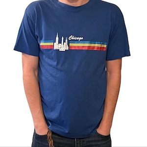 May include: A blue t-shirt with a graphic of the Chicago skyline and the word "Chicago" in white lettering. The graphic is surrounded by colorful stripes.