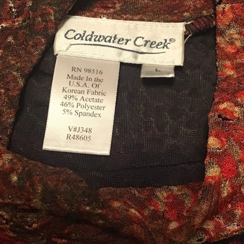 Pode incluir: Uma etiqueta branca com texto preto que diz "Coldwater Creek" e inclui as seguintes informa&ccedil;&otilde;es: RN 98516, Fabricado nos EUA de tecido coreano, 49% acetato, 46% poli&eacute;ster, 5% spandex, V#J348, R48605.