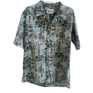 Puede incluir: Una camisa abotonada de manga corta con un estampado geométrico gris, blanco y verde azulado. El estampado incluye diseños de tortugas y flores. La camisa tiene cuello y un bolsillo delantero.