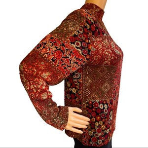 Pode incluir: Uma camisa de manga comprida com gola alta, com um padr&atilde;o vermelho, dourado e preto.