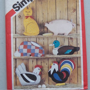 May include: A vintage sewing pattern for making five stuffed animal toys: a cat, pig, rabbit, duck, and rooster. The pattern is printed on a white background with a red border and the word "Simple" in black.