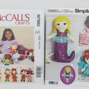 May include: Two sewing patterns for making dolls. The first pattern is for a mermaid doll with a purple tail and a blue top. The second pattern is for a fairy doll with blue wings and a turquoise dress. The patterns are from McCall's Crafts and Simplicity.
