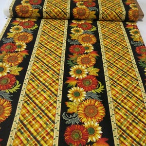 May include: Fabric roll featuring a repeating pattern of sunflowers and autumn leaves. The design includes vertical black stripes with floral arrangements and diagonal plaid sections in yellow, orange, and green. A cream-colored border with a leaf pattern frames the floral and plaid sections.