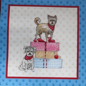 May include: A fabric square featuring a whimsical illustration of two dogs wearing red bandanas. One dog stands atop a stack of gift boxes, while the other sits below. The background is patterned with paw prints.