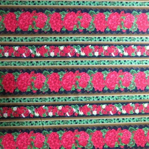 May include: Fabric with a repeating pattern of red geraniums and smaller red and white flowers on a navy blue background. The design includes green and gold stripes, creating a floral and striped pattern.