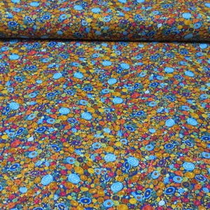 May include: A roll of fabric with a colorful floral pattern. The design features small, round shapes in shades of blue, yellow, orange, and red on a dark blue background. The fabric is likely cotton or a similar material.