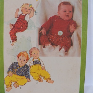 May include: A vintage sewing pattern for baby clothes. The pattern includes three different styles of baby outfits: a red and white patterned jumpsuit, a yellow jumpsuit with a blue bib, and a red and white patterned onesie with long sleeves.