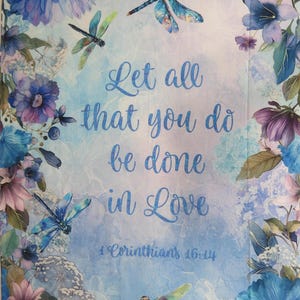 May include: A floral design with blue and purple flowers and dragonflies. The image has the text "Let all that you do be done in Love" and "1 Corinthians 16:14" in a script font.