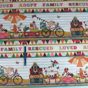May include: A colorful fabric featuring a repeating pattern of dogs in various settings. The design includes dogs riding in carts, on bicycles, and in suitcases, with the words "LOVED," "ADOPT," "FAMILY," and "RESCUED" displayed across the top and bottom.