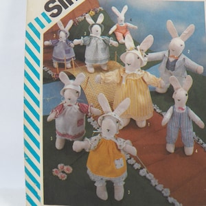 May include: A set of eight white bunny sewing patterns with different outfits. The bunnies are wearing dresses, overalls, and a suit. The patterns are numbered 1 through 8.