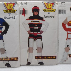 Op de afbeelding: Drie vintage Butterick naaipatronen voor VR Troopers kostuums. Elk patroon toont een ander personage: Ryan Steel, J.B. Reese en Kaitlin Star. De kostuums zijn in verschillende kleuren, waaronder blauw, wit, rood en zwart.