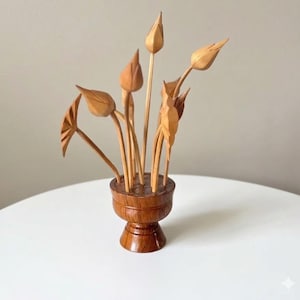 May include: A light brown wooden sculpture featuring several carved flower buds and leaves emerging from a small, round, pedestal-style wooden base. The natural wood grain is visible throughout the entire piece, showcasing a smooth, polished finish on the stems, petals, and the circular container.