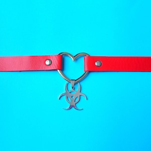 May include: Red leather choker with a silver heart-shaped pendant featuring a biohazard symbol.