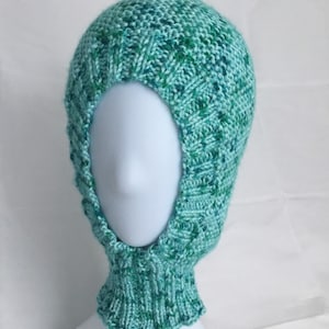 May include: A teal blue knitted balaclava with a green and blue marled pattern. The balaclava is on a white mannequin head.