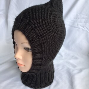 Puede incluir: Balaclava de punto negro con capucha puntiaguda. La balaclava está hecha de un material suave y cálido y cubre la cabeza y el cuello.