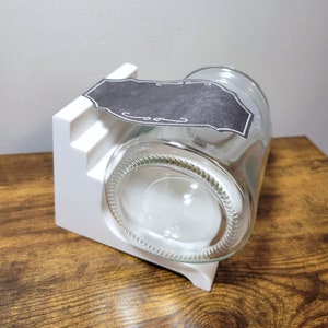 May include: White plastic jar holder with a clear glass jar with a black label that says "cooo".