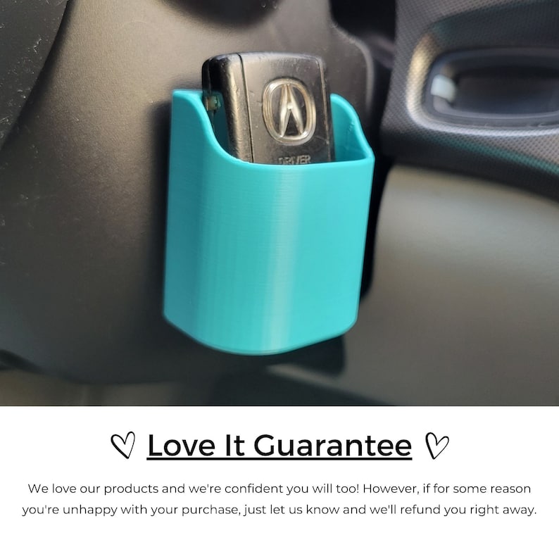 May include: A teal-colored, 3D-printed car key holder mounted on a car's dashboard. The holder is a small, open-topped container designed to hold a car key. The key has a silver Acura logo. The holder is attached to a black surface.