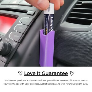 May include: A purple car phone holder with a lip balm tube inserted. The lip balm tube is blue and white with the text "ChapStick Skin Classic Original" on the label.