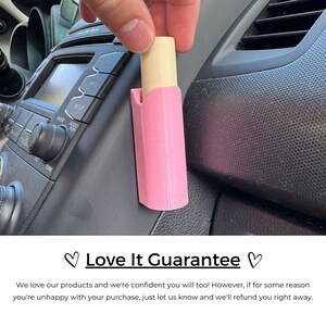 Op de afbeelding: Een roze plastic autotelefoonhouder met een beige telefoon erin. De houder is bevestigd aan het dashboard van een auto. Love It Guarantee.