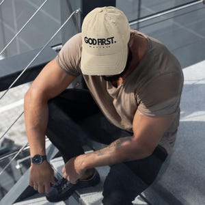 May include: A beige distressed baseball cap with black text that reads "GOD FIRST. MATTHEW 6:33".