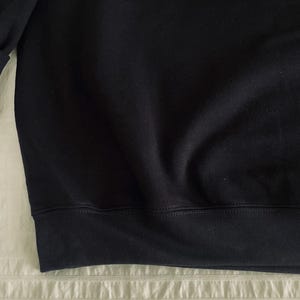 Op de afbeelding: Zwart sweatshirt met geribbelde zoom en manchetten. De rechterbovenhoek heeft een patch met de tekst "Mickey Mouse" in een decoratief lettertype. Het sweatshirt is gemaakt van een zachte, donkere stof.
