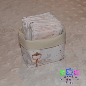 Può includere: Un piccolo cestino color crema pieno di cuscinetti quadrati di tessuto fantasia. Il cestino ha un bordo in similpelle beige chiaro e un esterno in tessuto bianco decorato con un motivo a libellula e chiave in oro. I cuscinetti hanno un motivo simile.