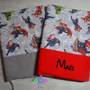 Peut inclure: Deux protège-livres avec des motifs de super-héros. L'un est gris et l'autre rouge. Les couvertures présentent un motif de divers super-héros sur un fond gris. Le protège-livre rouge porte le nom "Maël" en noir.