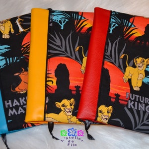 Peut inclure: Couvertures de cahiers avec des dos colorés et un tissu sur le thème du Roi Lion. Les couvertures présentent Simba, Timon et Pumbaa sur fond de coucher de soleil. Les dos sont bleus, jaunes et rouges.