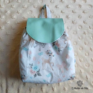 May include: A white backpack with a mint green flap, featuring a pattern of deer, flowers, bows, and butterflies. The backpack has a top handle and adjustable straps, perfect for carrying books and supplies.