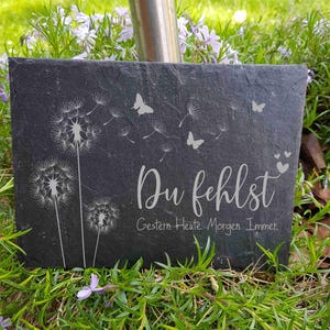 Könnte beinhalten: Eine schwarze Schiefertafel mit einem weißen Löwenzahnmuster und dem Text "Du fehlst" (Du fehlst) mit den Worten "Gestern. Heute. Morgen. Immer." (Gestern. Heute. Morgen. Immer) darunter.