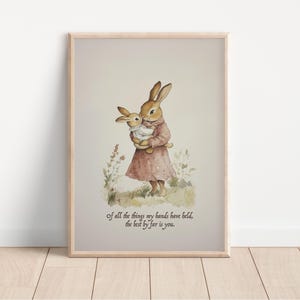May include: Watercolor print of two rabbits, one holding the other. The rabbits are in a field of grass and flowers. The print is in a wooden frame. Text at the bottom reads: "of all the things my hands have held, the best by far is you."