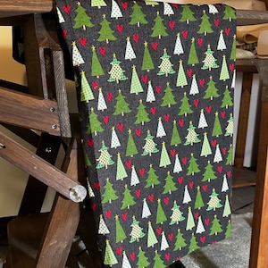 May include: Black fabric with a repeating pattern of green Christmas trees and red hearts. The fabric is folded and draped over a wooden chair.