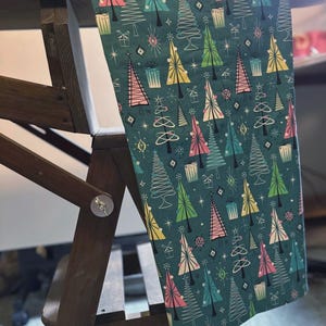 Puede incluir: Una tela azul verdosa con un patr&oacute;n repetitivo de &aacute;rboles de Navidad estilizados en rosa, verde y amarillo. Los &aacute;rboles est&aacute;n delineados en blanco y tienen un dise&ntilde;o retro.