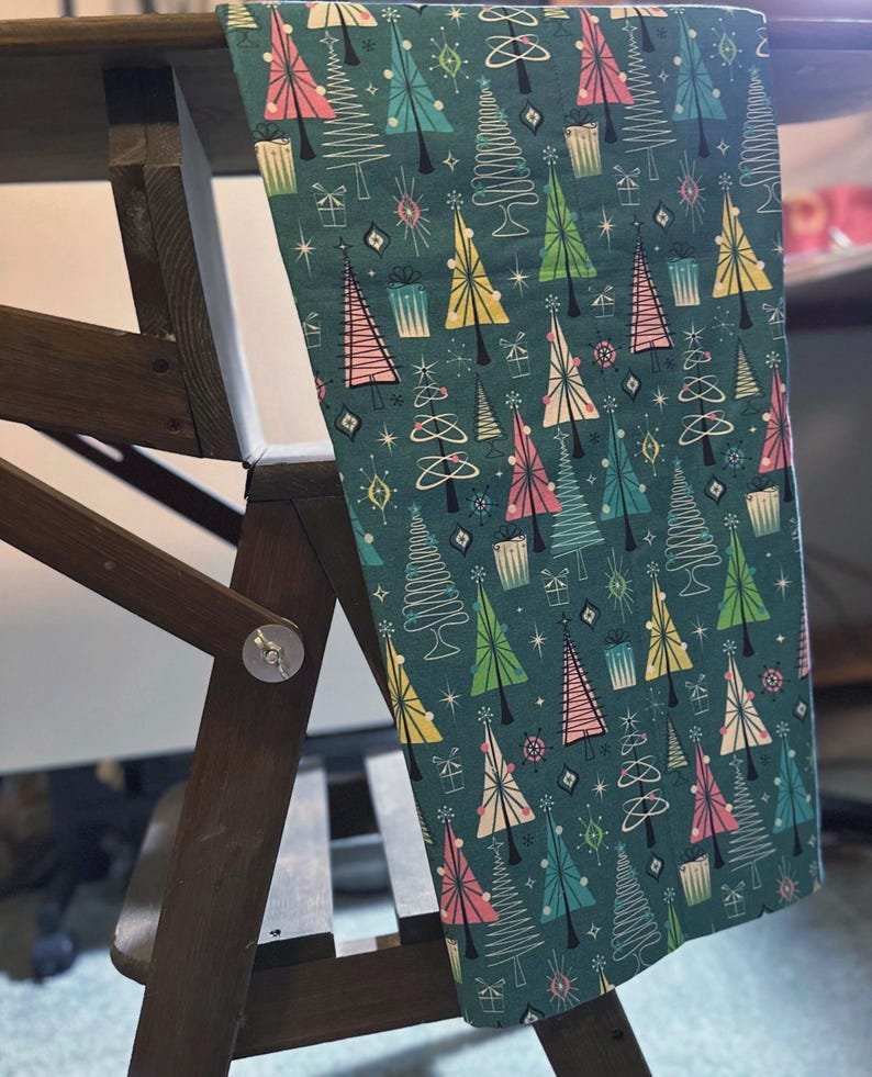 Puede incluir: Una tela azul verdosa con un patr&oacute;n repetitivo de &aacute;rboles de Navidad estilizados en rosa, verde y amarillo. Los &aacute;rboles est&aacute;n delineados en blanco y tienen un dise&ntilde;o retro.