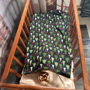 May include: A wooden crib with a white and green Christmas tree patterned blanket and a stuffed giraffe toy inside.